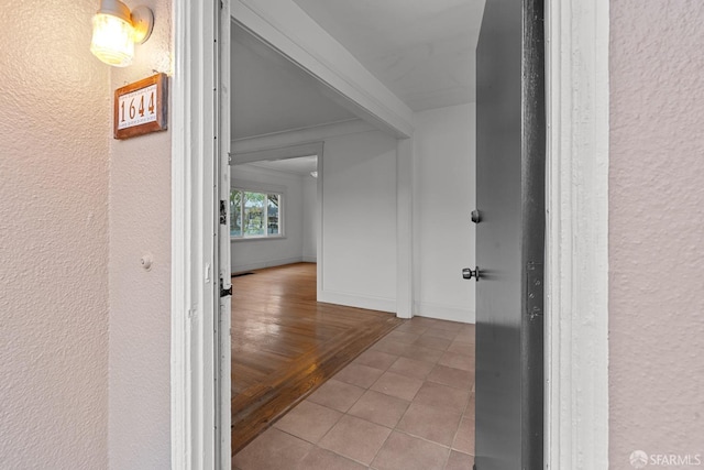 hall with crown molding, a textured wall, baseboards, and light tile patterned floors