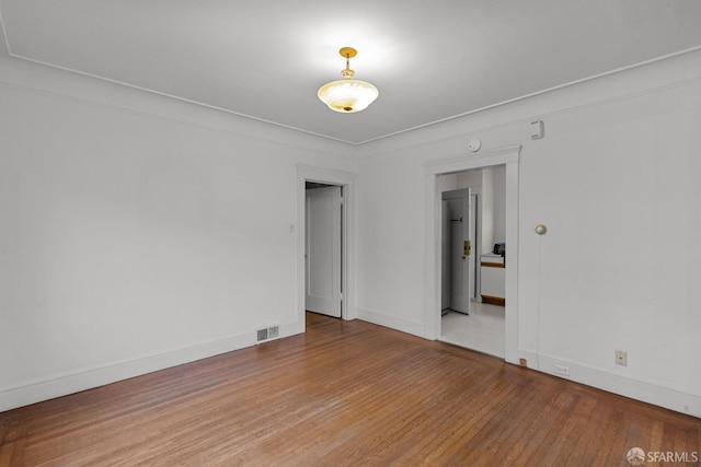 empty room with baseboards, visible vents, and wood finished floors