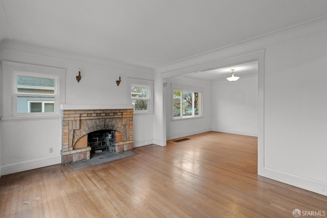 unfurnished living room featuring light wood-style flooring, a fireplace, visible vents, baseboards, and ornamental molding