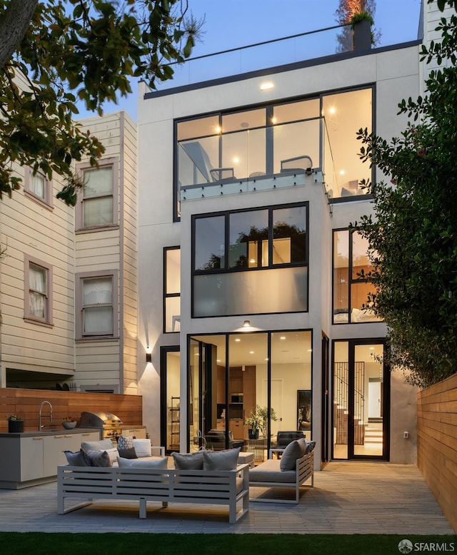 back of house featuring a balcony, outdoor lounge area, exterior kitchen, and sink