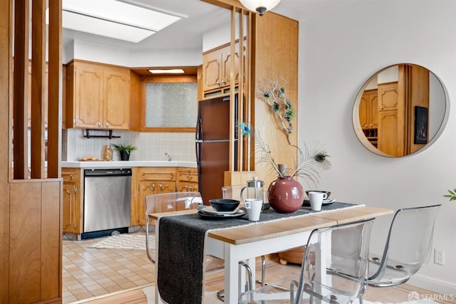 kitchen with light countertops, stainless steel dishwasher, freestanding refrigerator, and tasteful backsplash