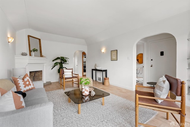 living room featuring arched walkways, a fireplace with raised hearth, vaulted ceiling, and baseboards