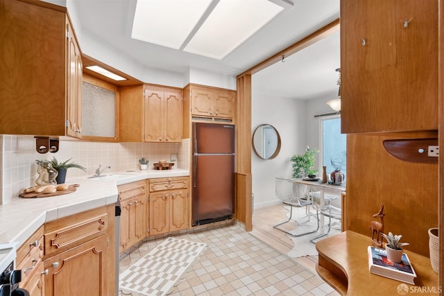 kitchen with tile countertops, a sink, baseboards, backsplash, and freestanding refrigerator