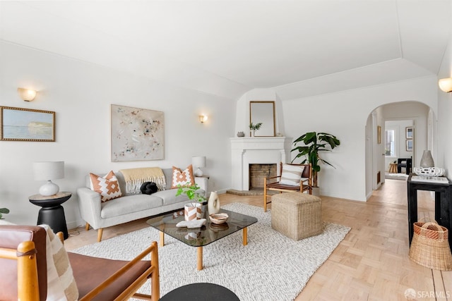 living area with arched walkways, a fireplace with raised hearth, lofted ceiling, and baseboards