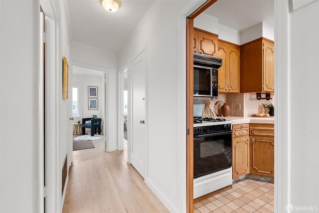 kitchen with tile countertops, gas range oven, light wood-style floors, black microwave, and backsplash