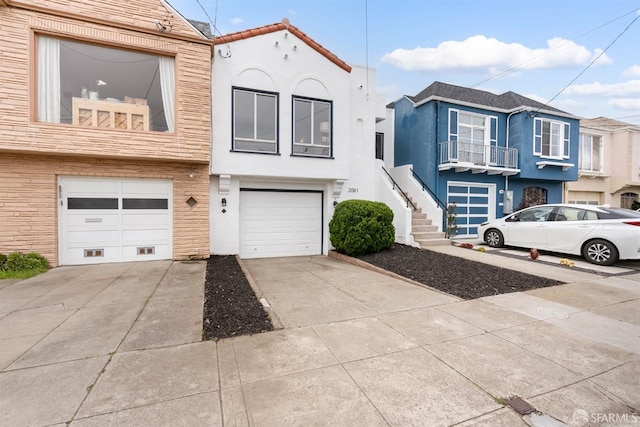 multi unit property with concrete driveway, stairway, an attached garage, and stucco siding