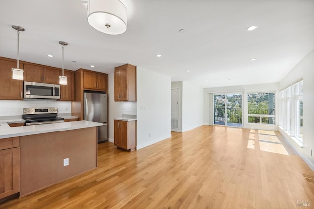 kitchen with backsplash, light wood-type flooring, hanging light fixtures, and appliances with stainless steel finishes