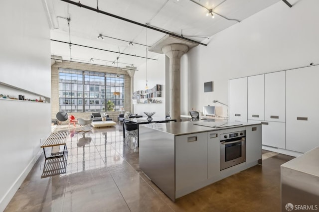 kitchen featuring white cabinets, a kitchen island, oven, and a high ceiling