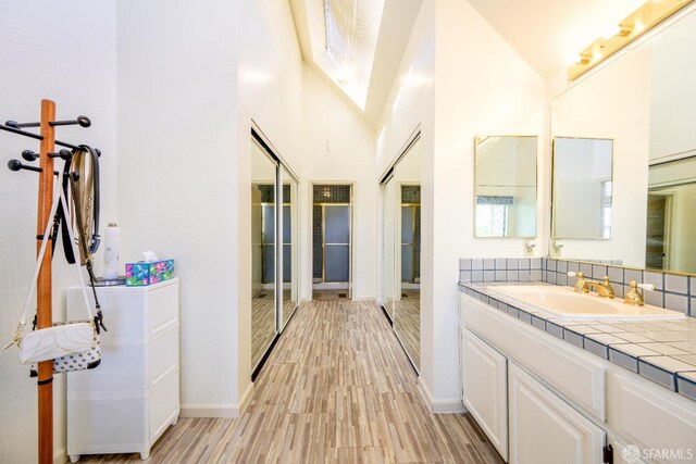 full bathroom with wood finished floors, baseboards, vanity, high vaulted ceiling, and backsplash