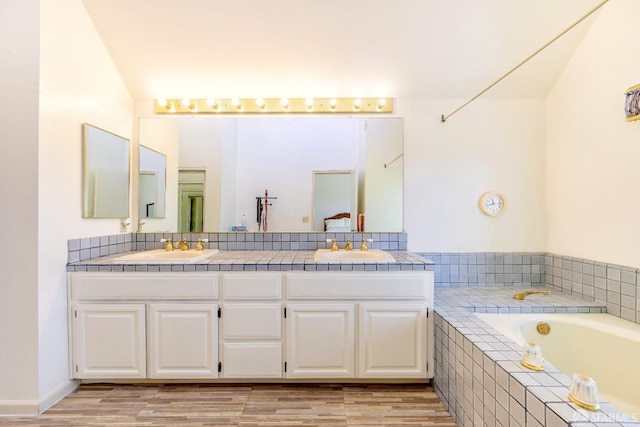 full bath with double vanity, wood finished floors, and tiled tub