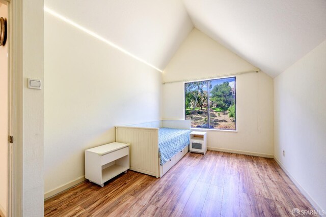 unfurnished bedroom featuring light wood-style flooring, lofted ceiling, and baseboards
