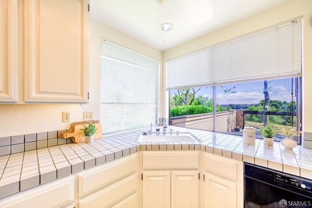 kitchen with black dishwasher, tile countertops, a sink, and white cabinets