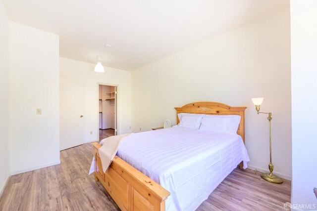 bedroom featuring light wood-style flooring, baseboards, and a walk in closet