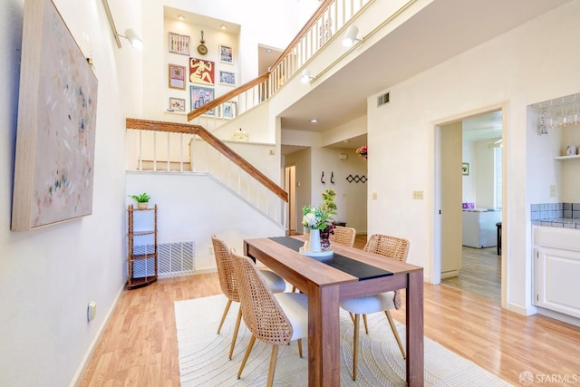 dining space with stairs, light wood-style flooring, baseboards, and a towering ceiling