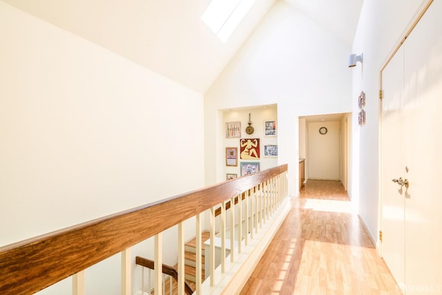 corridor featuring a skylight, high vaulted ceiling, light wood-style floors, and an upstairs landing