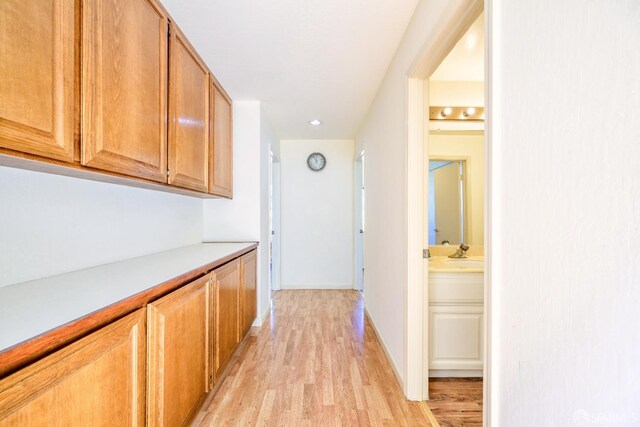 hallway with light wood finished floors, a sink, baseboards, and recessed lighting