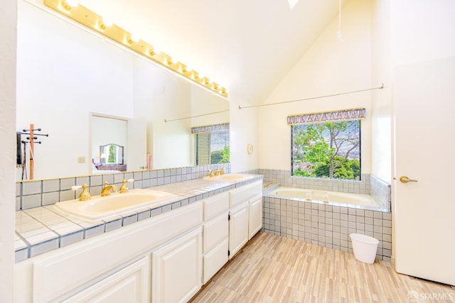 bathroom with a garden tub, wood finished floors, double vanity, and high vaulted ceiling