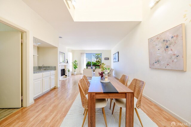 dining room with light wood-style floors, a fireplace, and baseboards