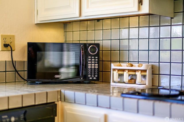 kitchen view of black microwave, decorative backsplash, and white cabinets