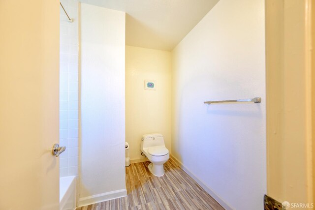 bathroom featuring toilet, wood finished floors,  shower combination, and baseboards