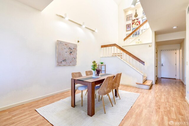 dining space featuring wood finished floors, stairs, baseboards, and a high ceiling