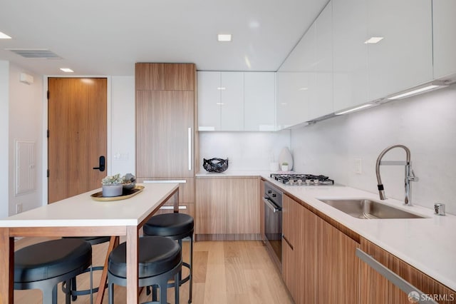 kitchen with a breakfast bar, white cabinets, stainless steel appliances, light hardwood / wood-style flooring, and sink