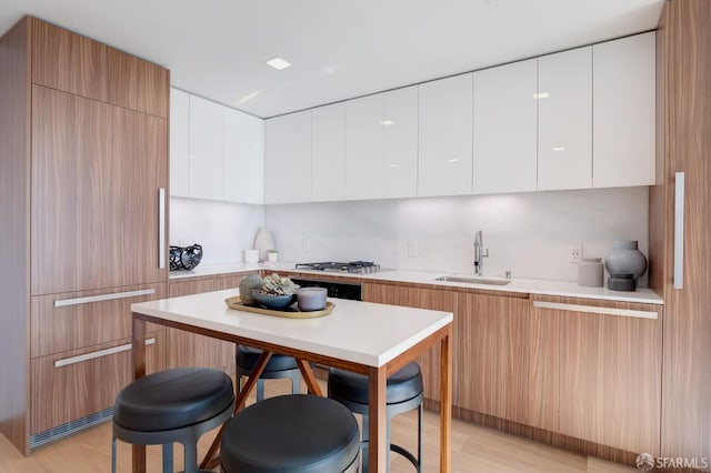 kitchen with light wood-type flooring, stainless steel gas stovetop, white cabinetry, and sink