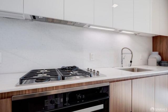 kitchen featuring stainless steel gas stovetop, oven, white cabinetry, and sink