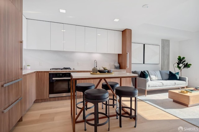 kitchen with white cabinets, a breakfast bar area, appliances with stainless steel finishes, and light wood-type flooring