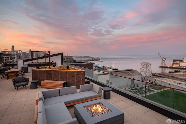 patio terrace at dusk with a balcony, an outdoor living space with a fire pit, and a water view