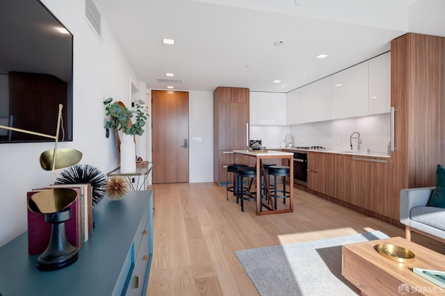 kitchen with tasteful backsplash, a kitchen island, white cabinetry, a kitchen breakfast bar, and light wood-type flooring