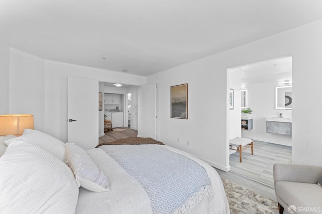 bedroom with washer and clothes dryer, light wood-type flooring, ensuite bath, and baseboards