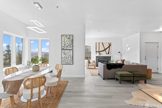 dining space featuring baseboards, light wood-type flooring, an inviting chandelier, and a glass covered fireplace