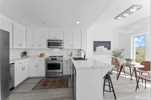 kitchen with a peninsula, a sink, light wood-type flooring, and stainless steel appliances