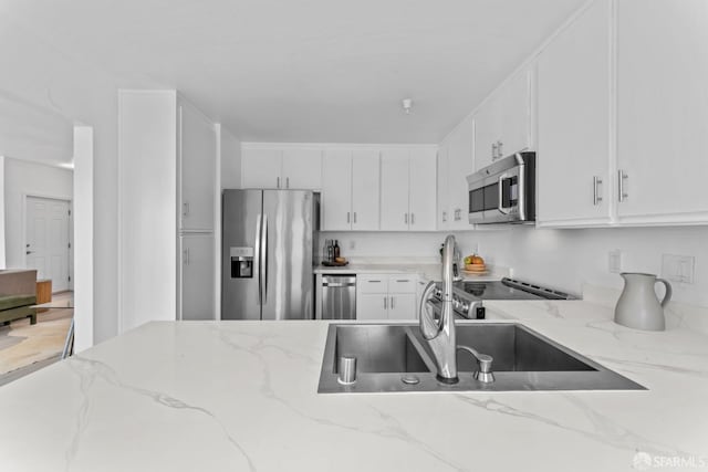 kitchen with light stone countertops, white cabinetry, a sink, and appliances with stainless steel finishes
