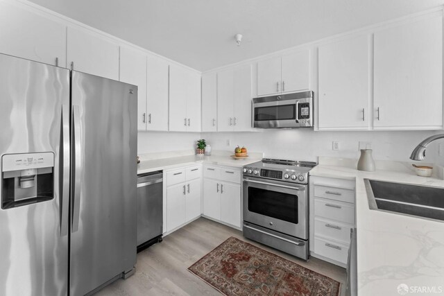 kitchen with stainless steel appliances, light wood-style floors, white cabinetry, and a sink