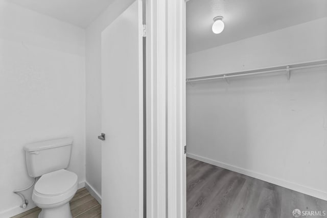 bathroom featuring toilet, wood finished floors, baseboards, and a walk in closet
