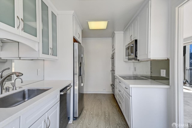 kitchen with white cabinetry, stainless steel appliances, light wood-type flooring, ornamental molding, and sink