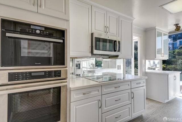 kitchen with ornamental molding, white cabinets, appliances with stainless steel finishes, and light wood-type flooring