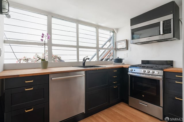 kitchen featuring butcher block countertops, a sink, stainless steel appliances, light wood finished floors, and dark cabinets