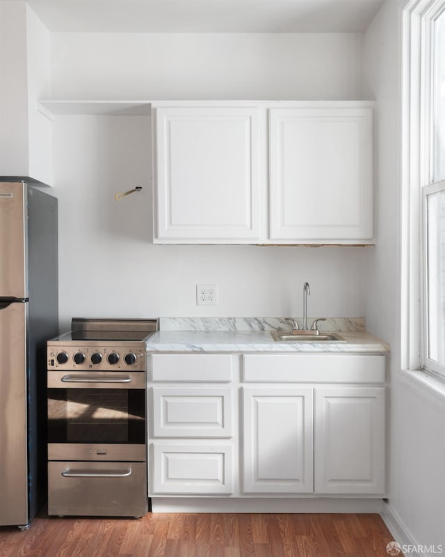 kitchen featuring a sink, stainless steel appliances, light wood-style floors, white cabinets, and baseboards