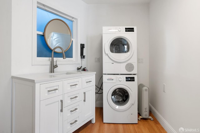 laundry area with baseboards, stacked washer and dryer, light wood-style flooring, cabinet space, and a sink