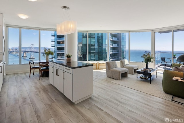 kitchen featuring white cabinets, light wood-style floors, a water view, dark countertops, and open floor plan