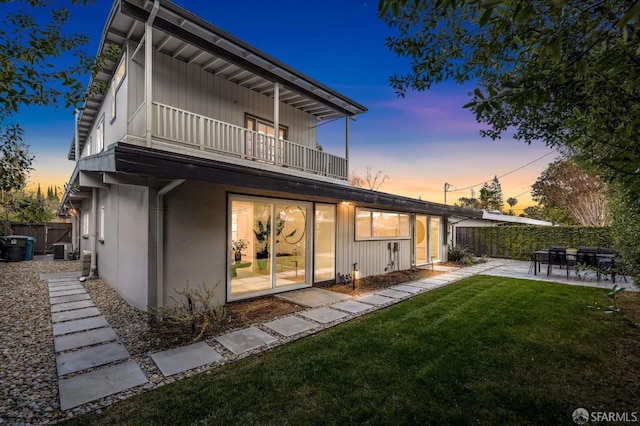 back of property at dusk with a patio, cooling unit, fence, and a balcony