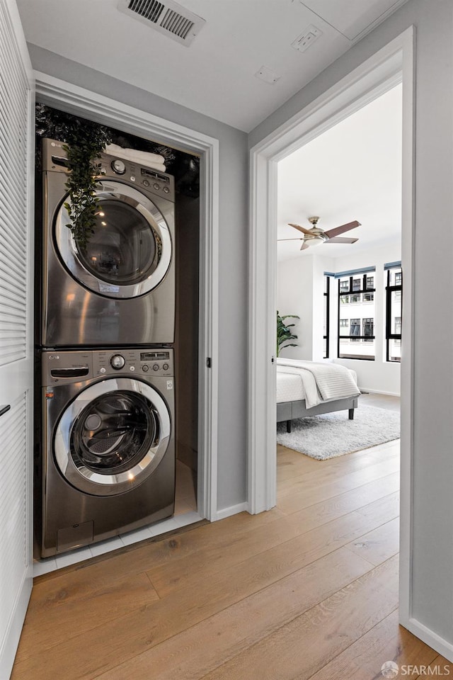 washroom featuring ceiling fan, stacked washer and dryer, and light hardwood / wood-style floors