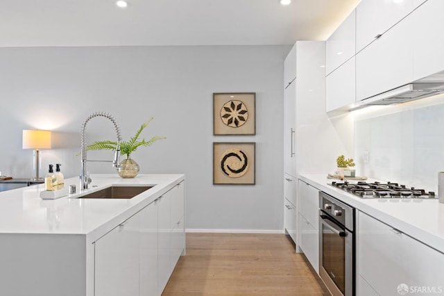 kitchen with sink, stainless steel appliances, a kitchen island with sink, white cabinets, and light wood-type flooring