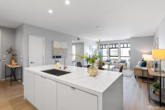 kitchen with sink, an island with sink, light hardwood / wood-style floors, light stone counters, and white cabinetry