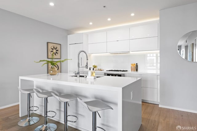 kitchen with white cabinetry, sink, a center island with sink, and light hardwood / wood-style flooring