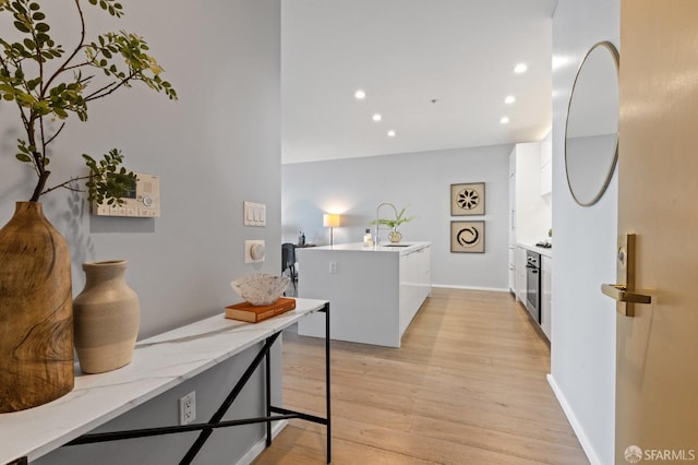 kitchen with white cabinetry, sink, light stone counters, light hardwood / wood-style flooring, and kitchen peninsula