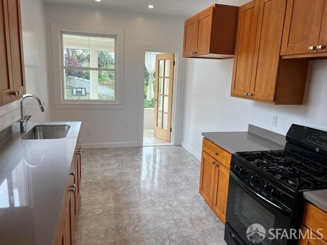 kitchen with black range with gas cooktop, a sink, brown cabinets, and baseboards